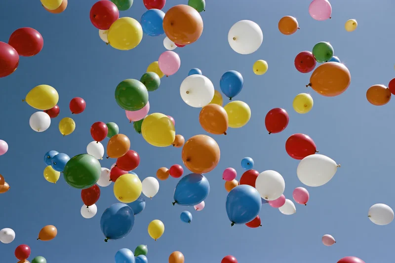 Multicolored balloons floating upward in open sky during celebration event