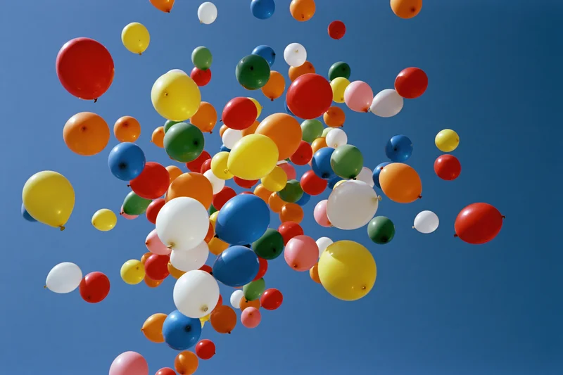 Multicolored balloons floating upward into clear blue sky