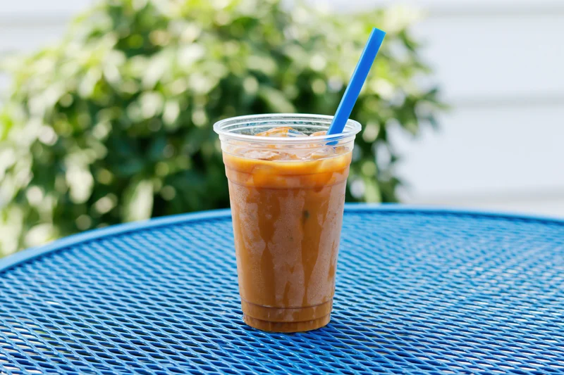 Iced coffee in a clear plastic cup with blue straw on a blue outdoor table