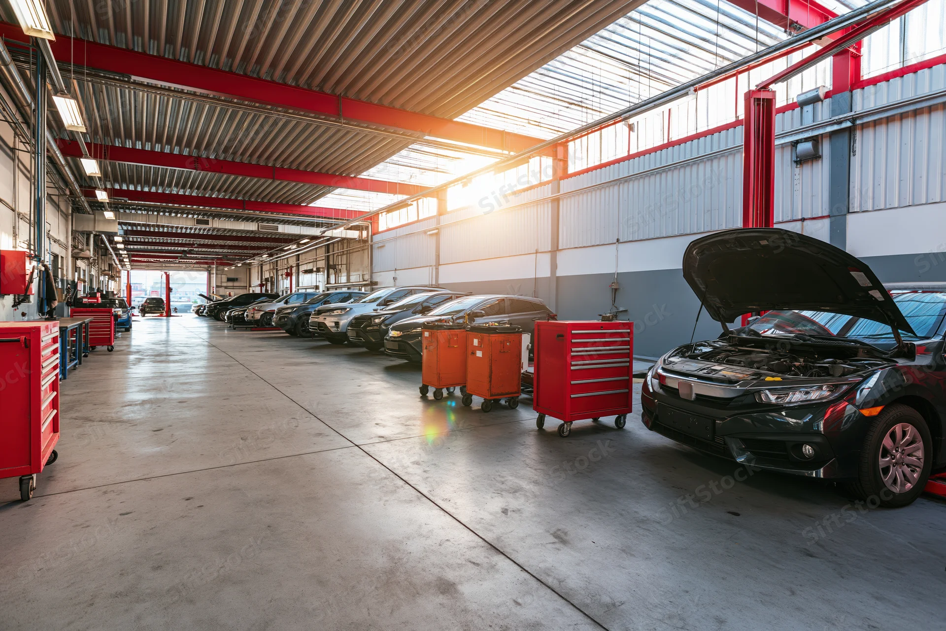 Black car with open hood in automotive service bay lined with vehicles and toolboxes