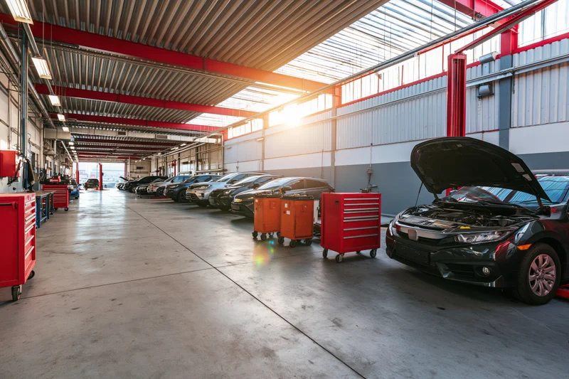 Black car with open hood in automotive service bay lined with vehicles and toolboxes