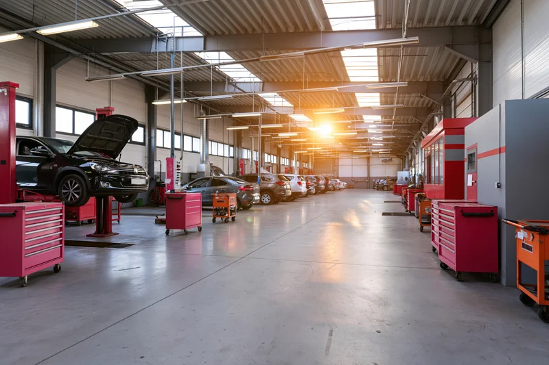 Automotive service bay interior with black car on lift and row of vehicles under skylight lighting