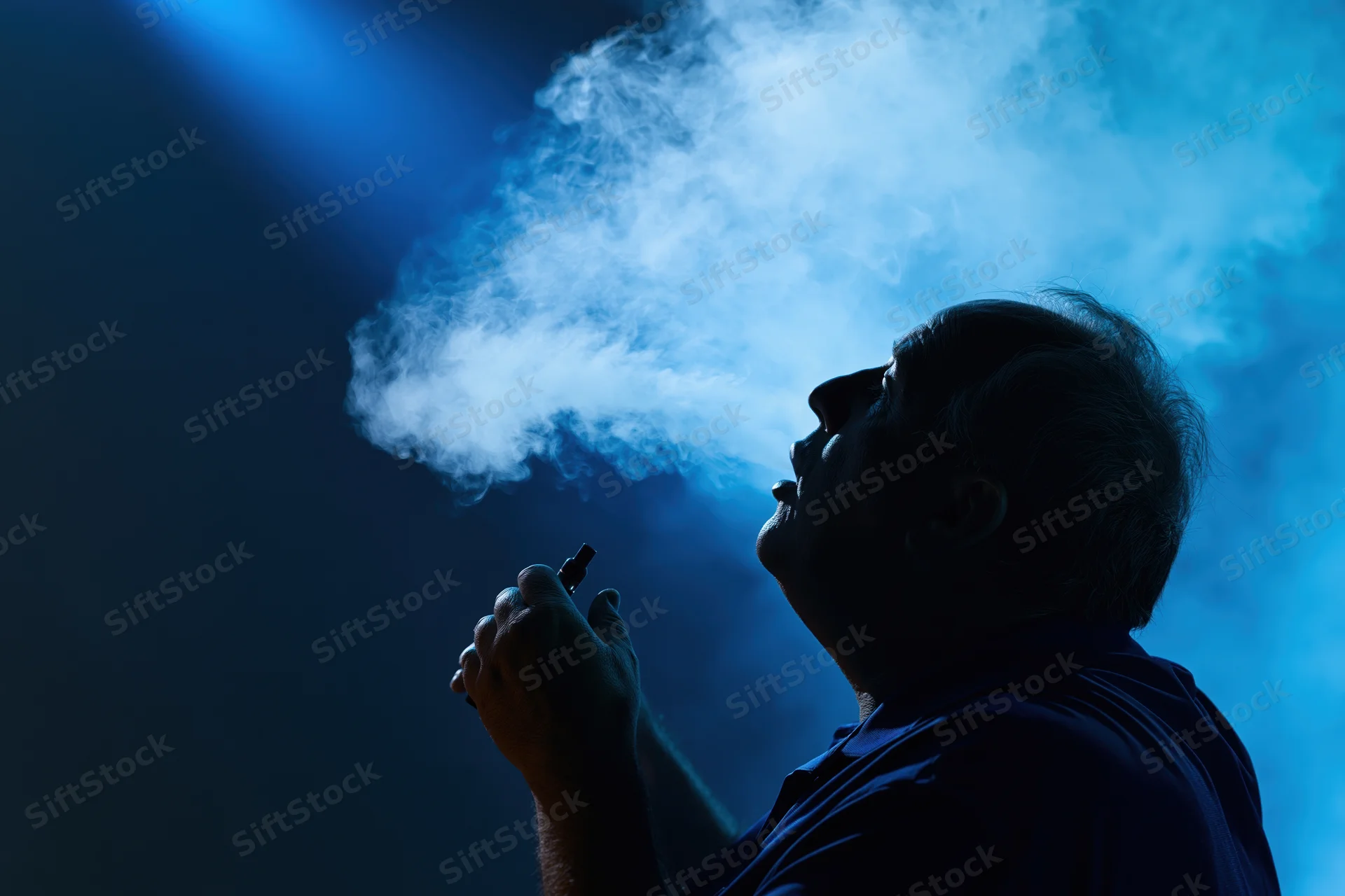 Man exhaling vapor from e-cigarette in dark blue light, silhouetted profile view