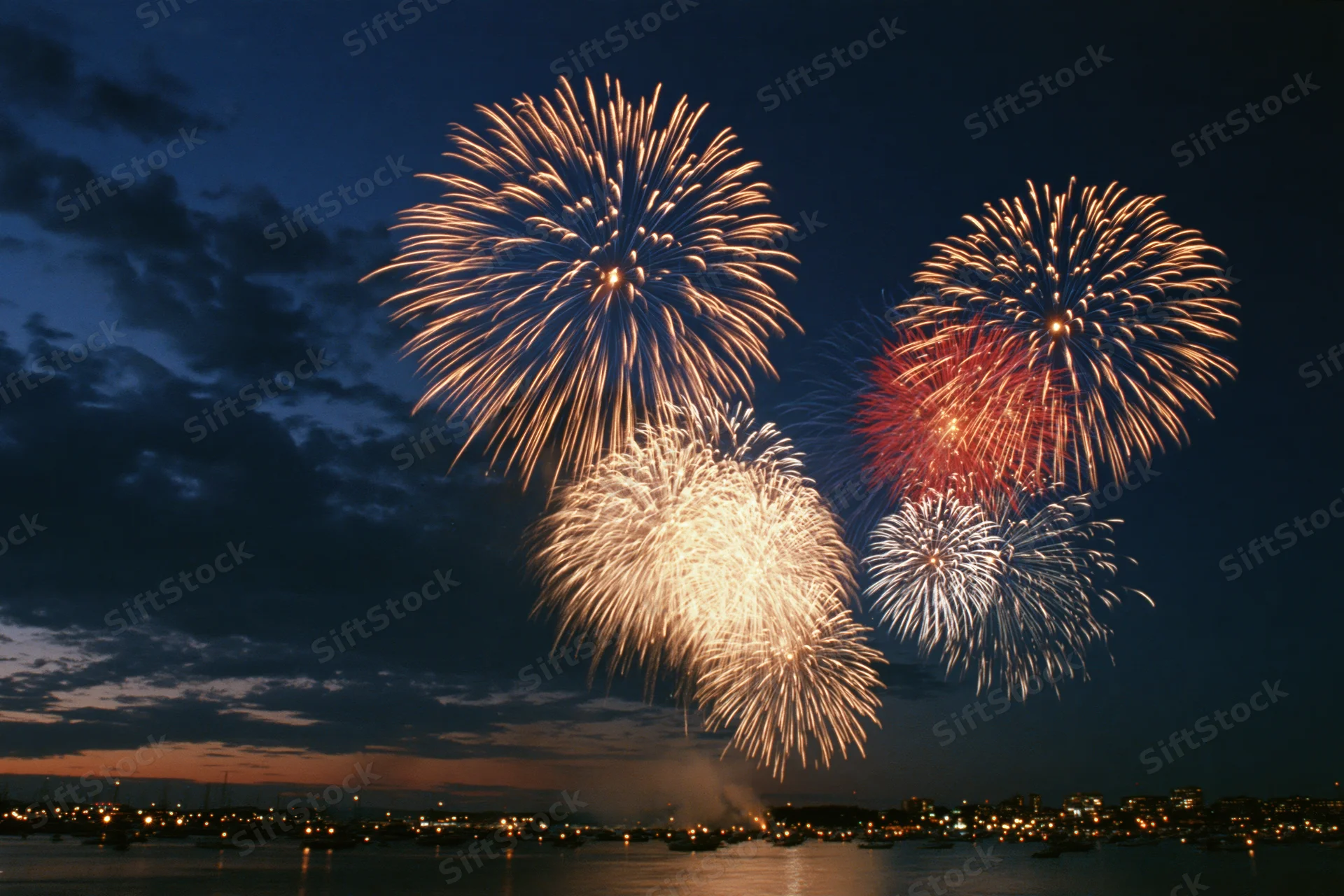 Fireworks bursting over a dark harbor at night with city lights reflecting on the water