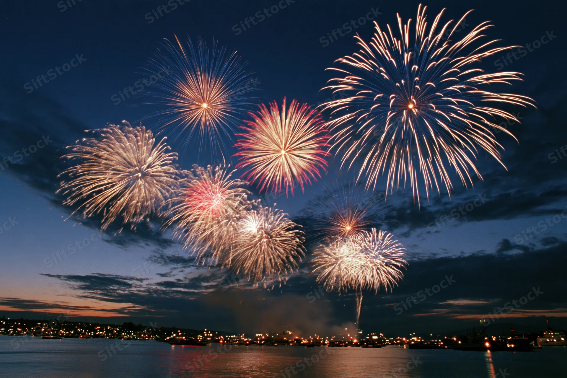 Fireworks bursting over a dark harbor at night with city lights reflecting on the water