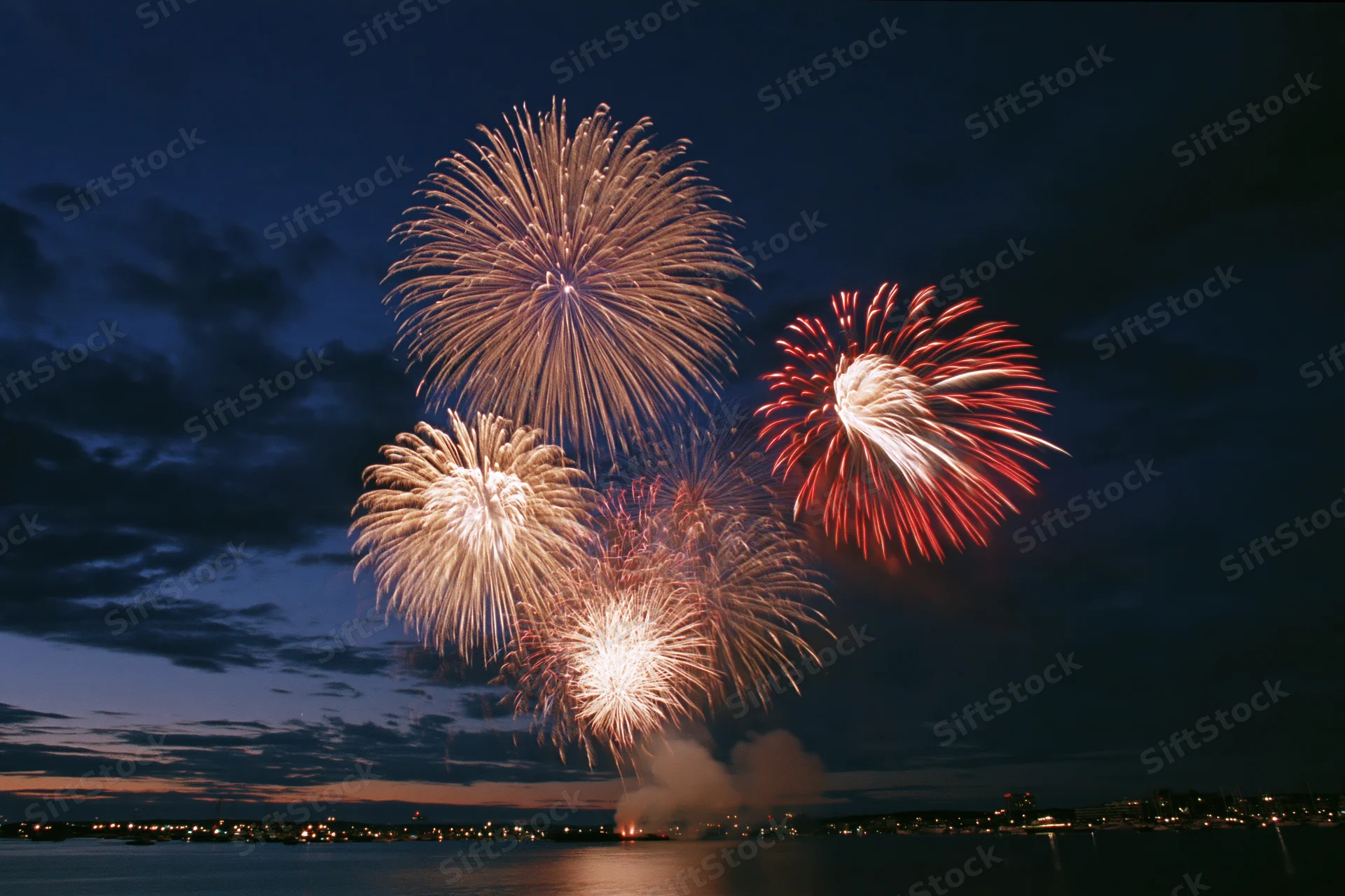 Fireworks bursting over a dark harbor at night with city lights reflecting on the water