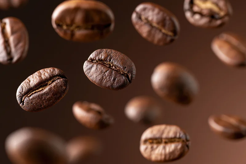Roasted coffee beans floating midair against a dark brown background