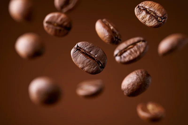 Roasted coffee beans floating midair against a dark brown background