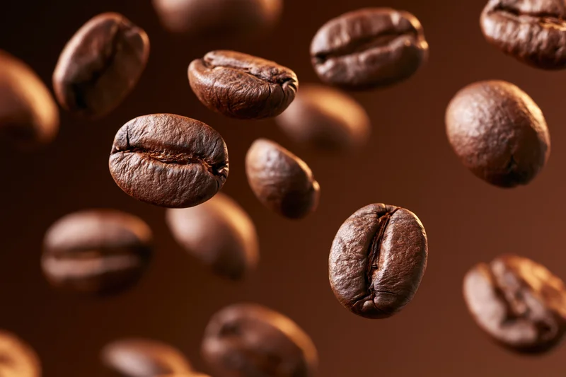 Roasted coffee beans floating midair against a warm brown background