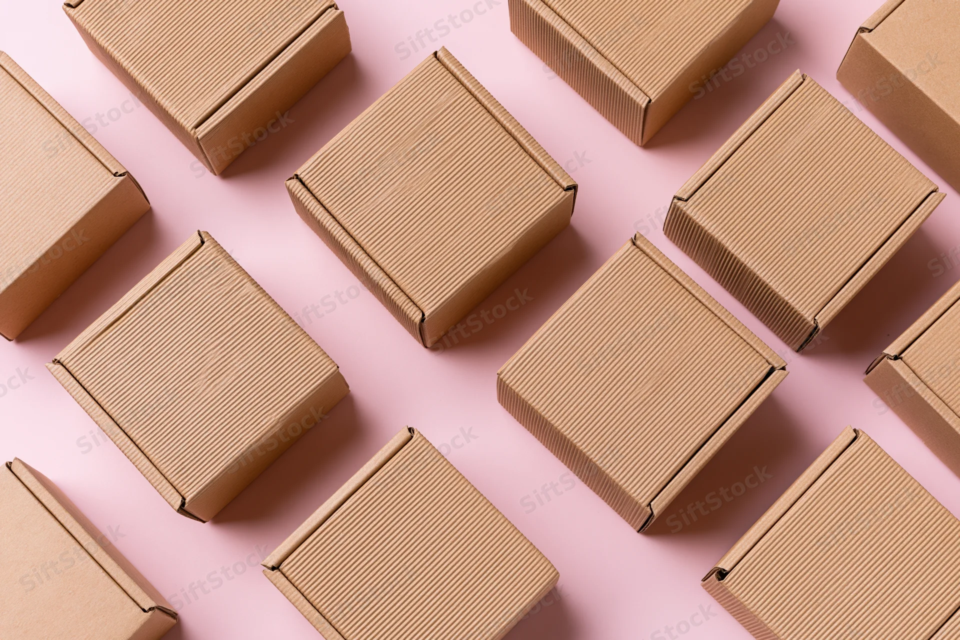 Multiple small closed kraft cardboard mailer boxes arranged in a pattern on a pink surface