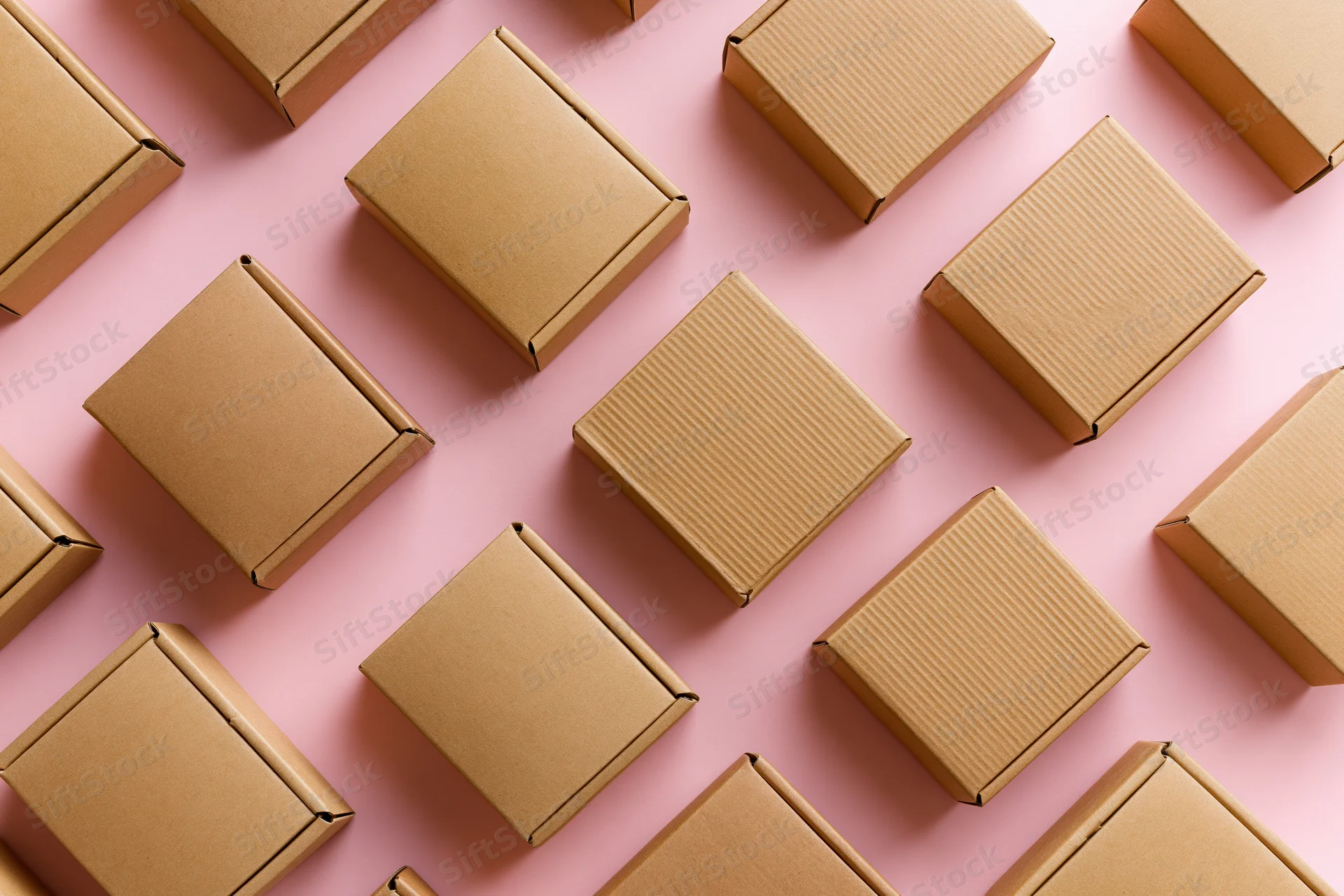 Multiple small closed kraft cardboard mailer boxes arranged in a grid pattern on a pink surface