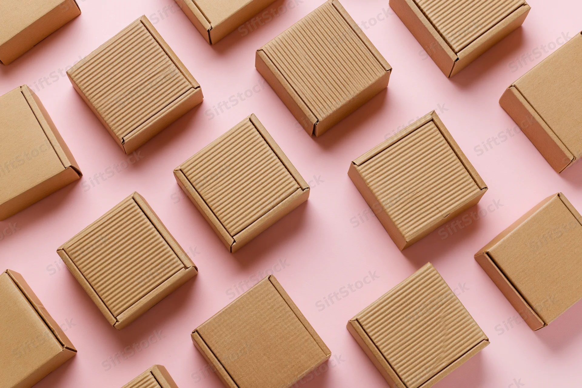Small closed kraft cardboard mailer boxes arranged in a pattern on a pink surface