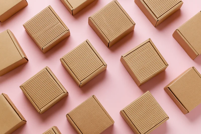 Small closed kraft cardboard mailer boxes arranged in a pattern on a pink surface