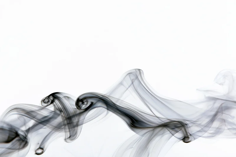 Dark smoke wisps curling and drifting upward against white background