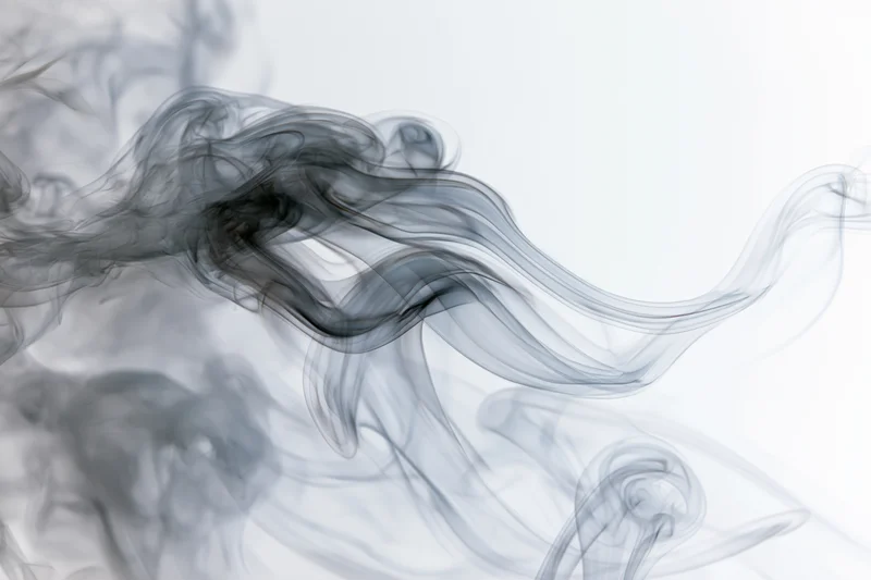Dark smoke wisps curling and drifting upward against a white background