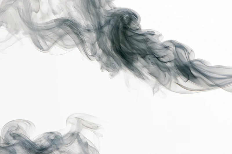 Dark smoke wisps curling and drifting upward against a white background