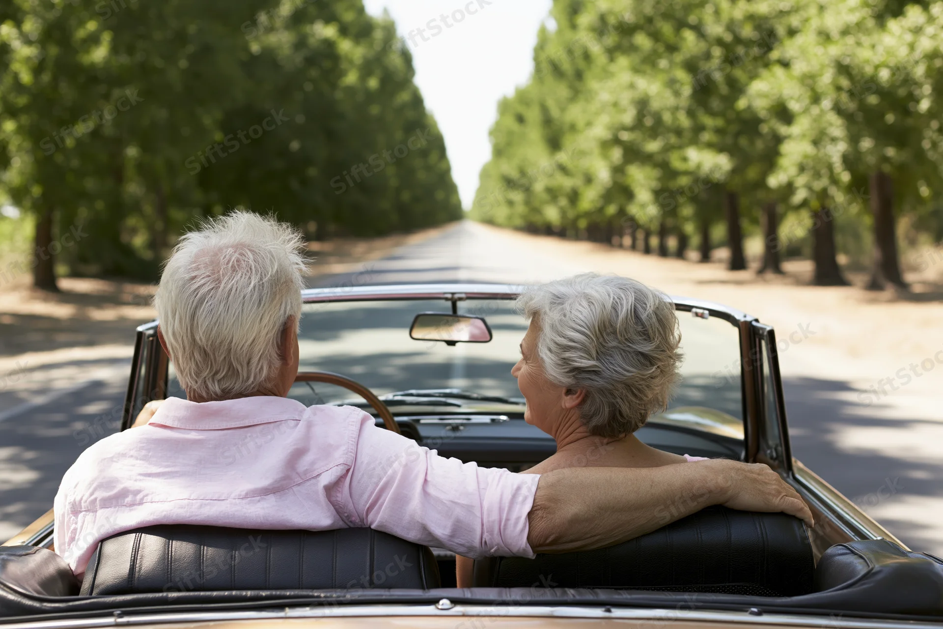 Senior couple driving vintage convertible on tree-lined road, seen from behind