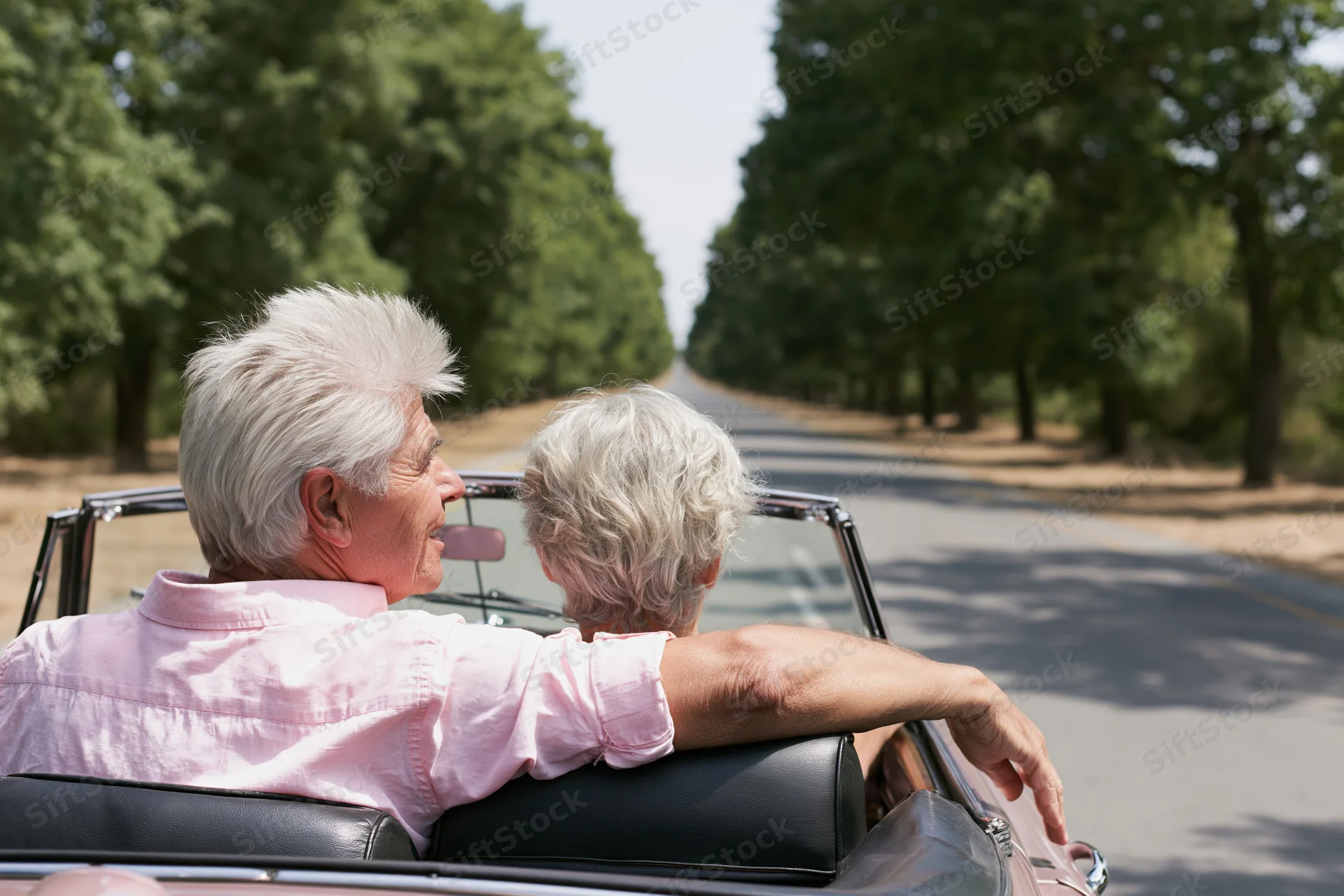 Senior couple driving vintage convertible on tree-lined road in summer