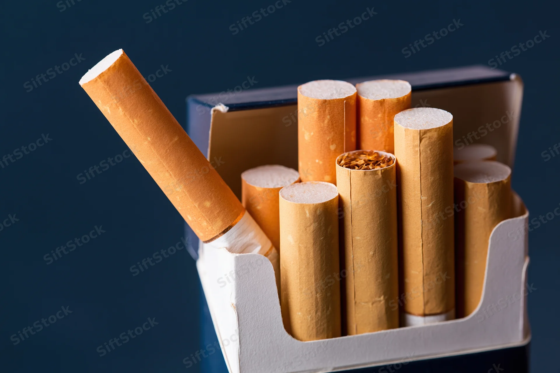 Open cigarette pack with one cigarette pulled out and angled against dark background