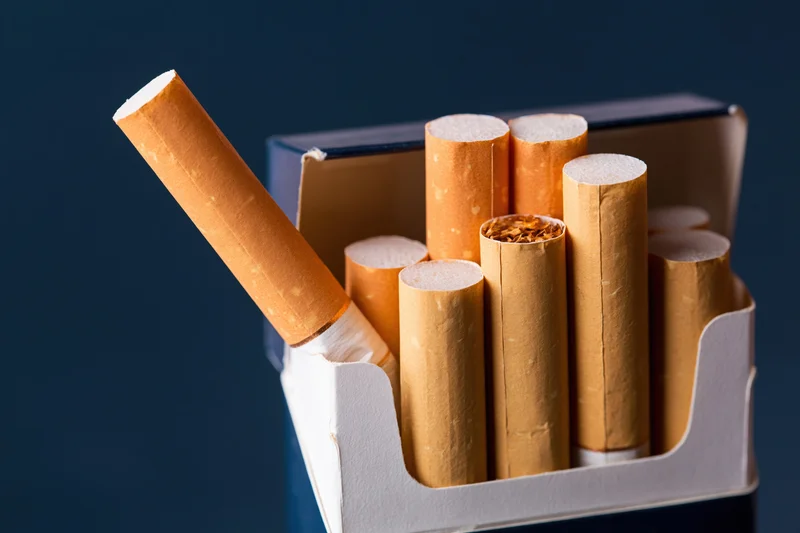 Open cigarette pack with one cigarette pulled out and angled against dark background