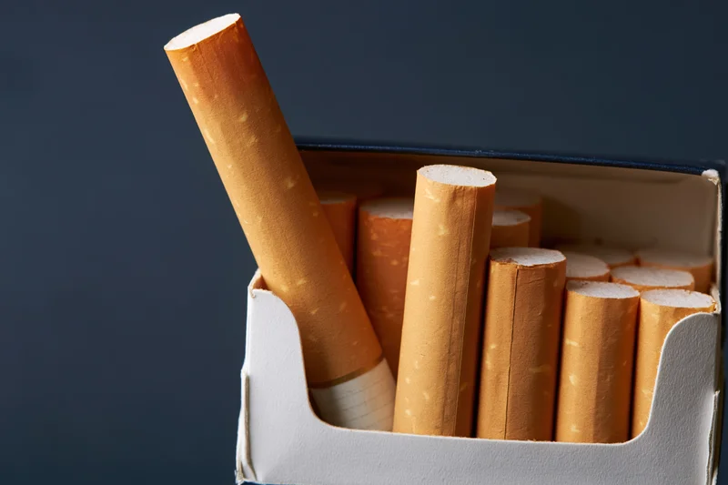 Open cigarette pack with one cigarette angled out against dark background