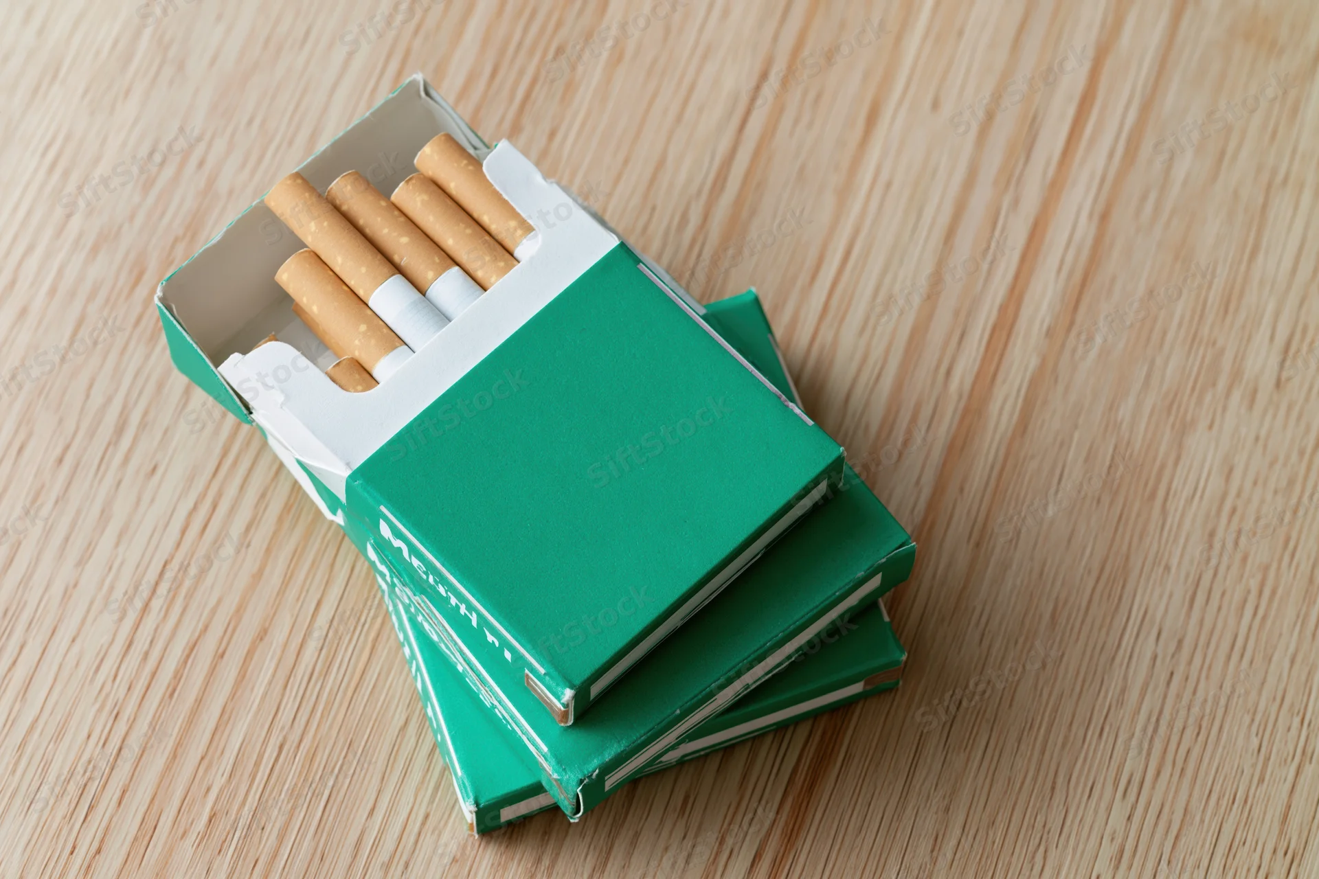 Open green menthol cigarette pack with several cigarettes visible on wooden table