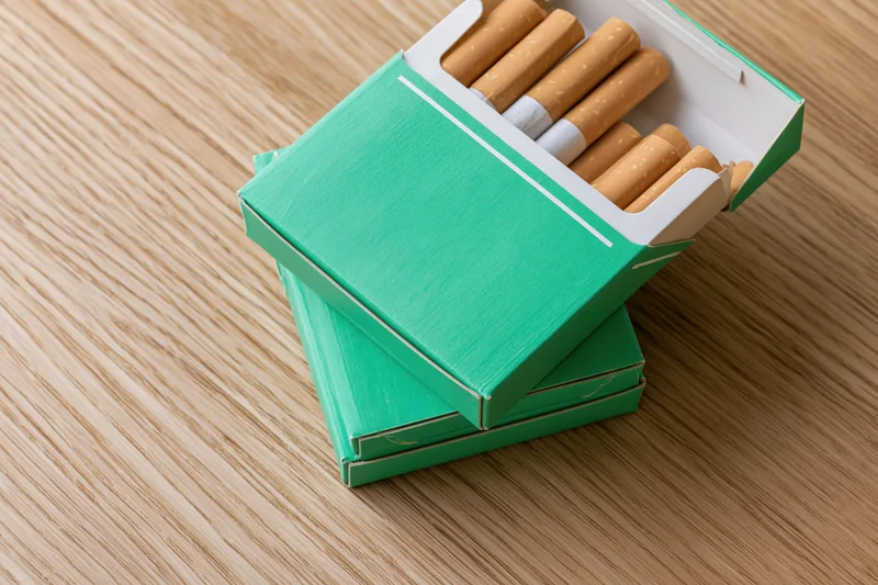 Open green cigarette pack with several cigarettes on wooden table