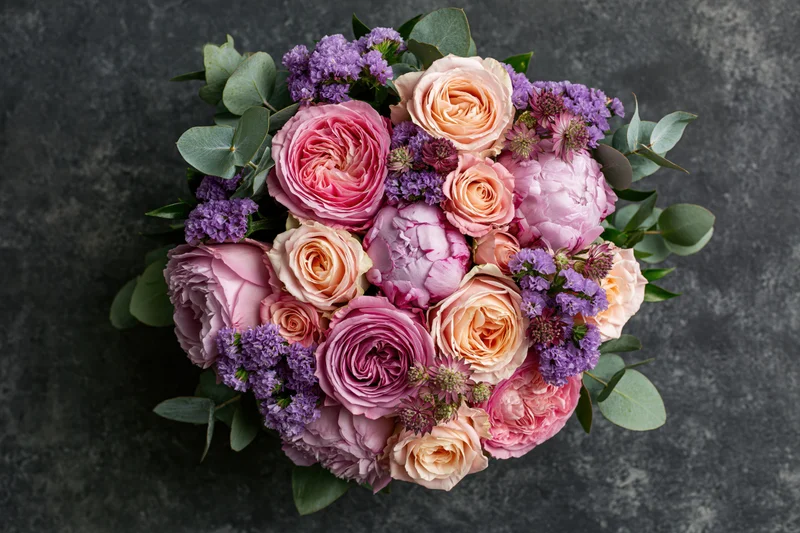 Overhead close-up of a lush mixed flower bouquet with pink roses, purple lavender, and green eucalyptus on dark textured surface