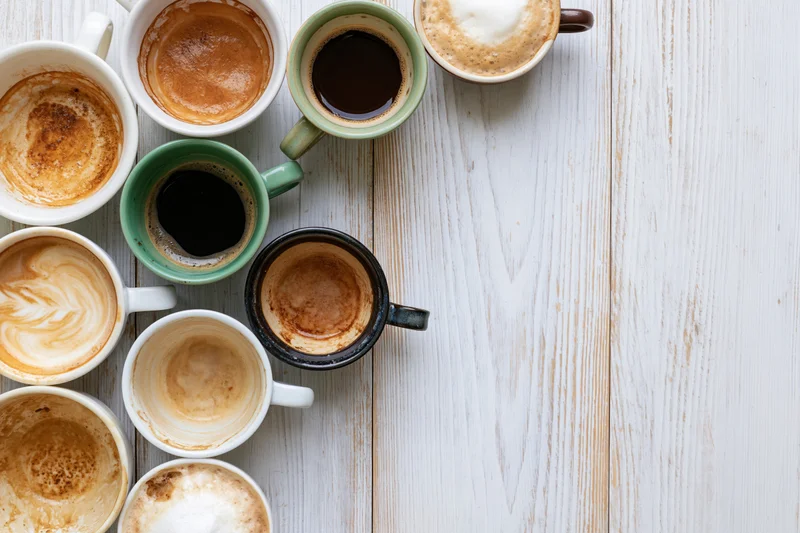 Overhead flat lay of assorted coffee cups with residue arranged on a white wooden table