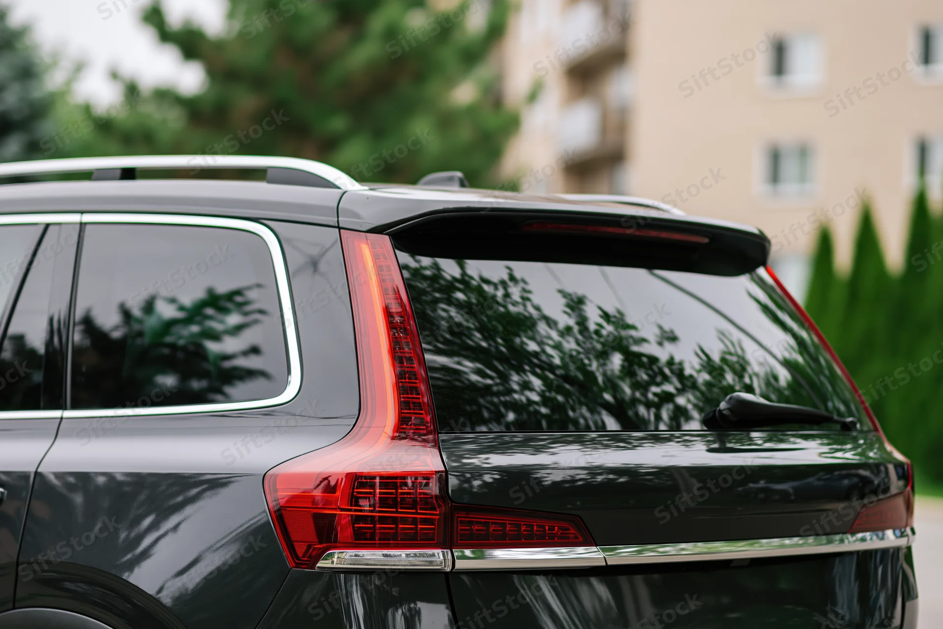Rear closeup of a black suv parked on a residential street with trees and apartment building in background