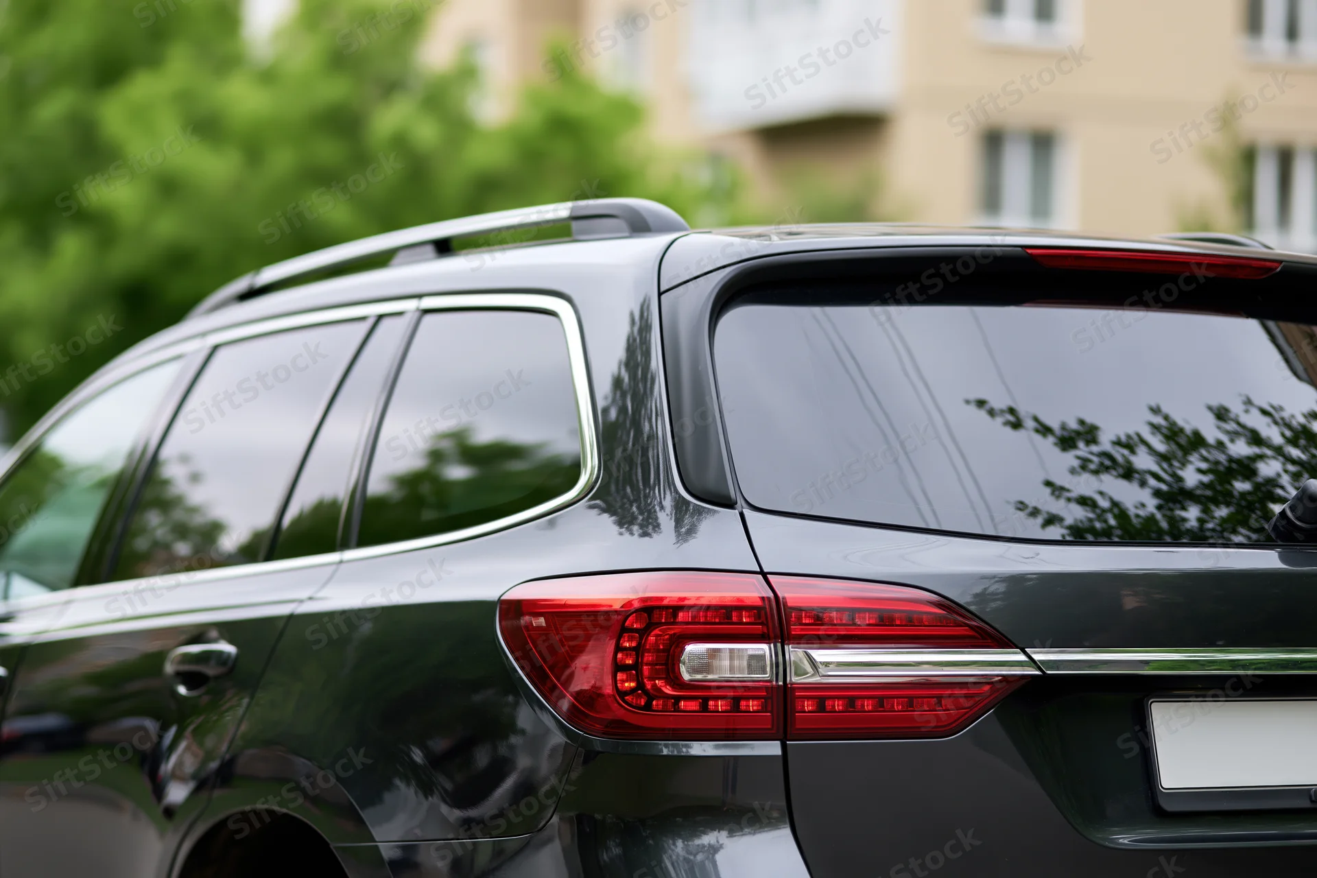 Rear closeup of a black suv parked on a residential street with trees and buildings in the background