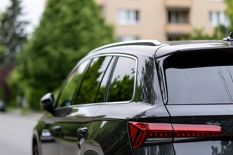 Rear closeup of a black suv parked on a residential street with trees and buildings in the background