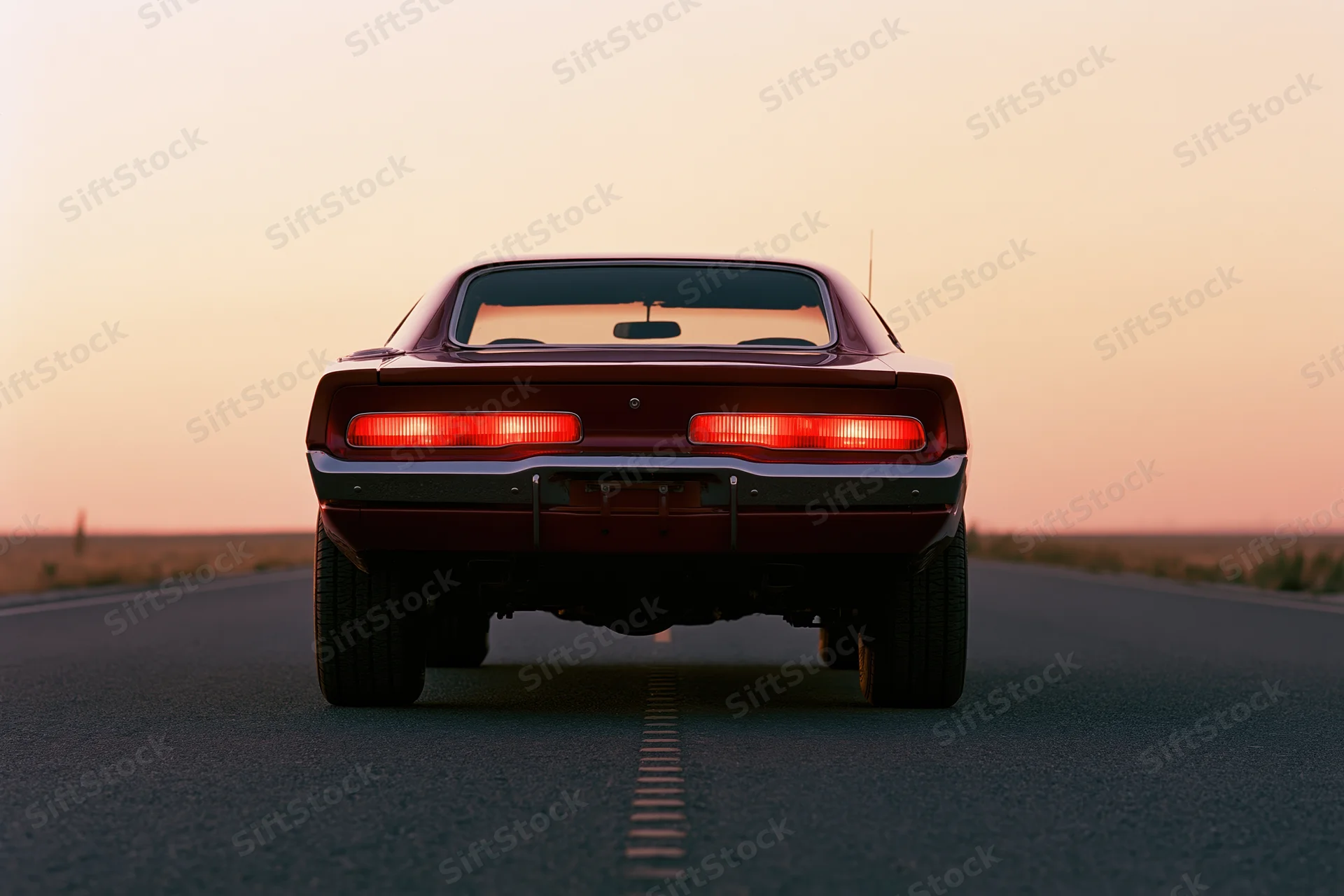 Rear view of a classic american muscle car with brake lights on a desert highway at sunset