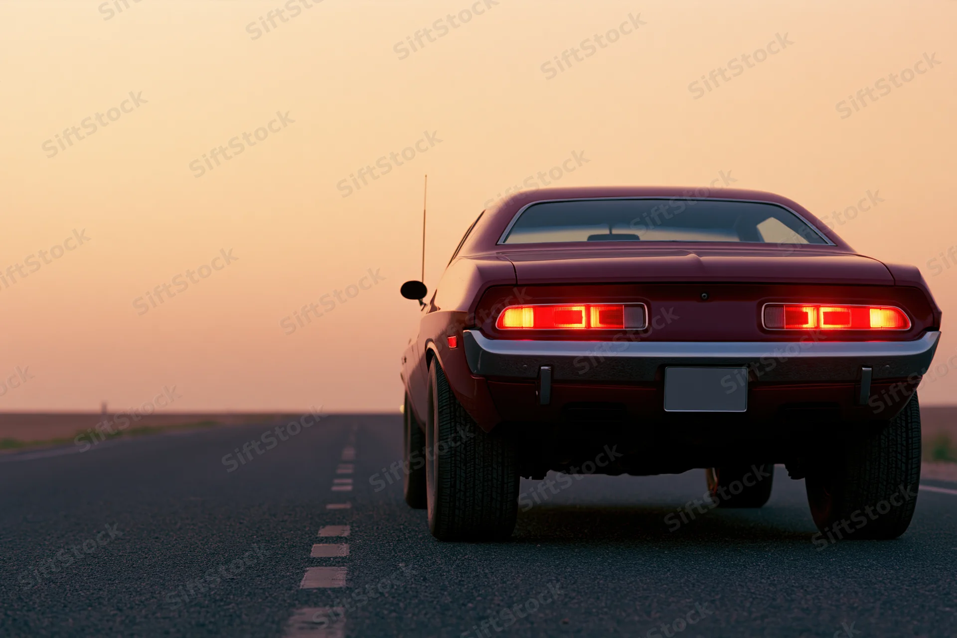 Rear view of a classic american muscle car driving on an open road at sunset