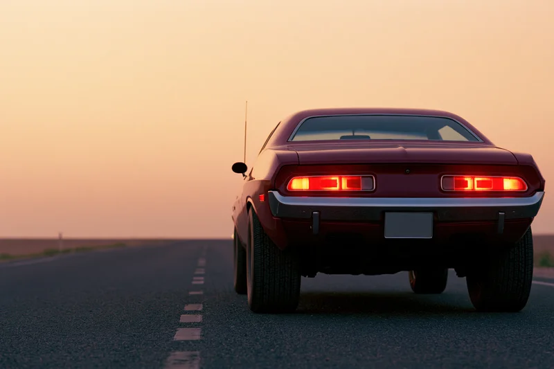 Rear view of a classic american muscle car driving on an open road at sunset