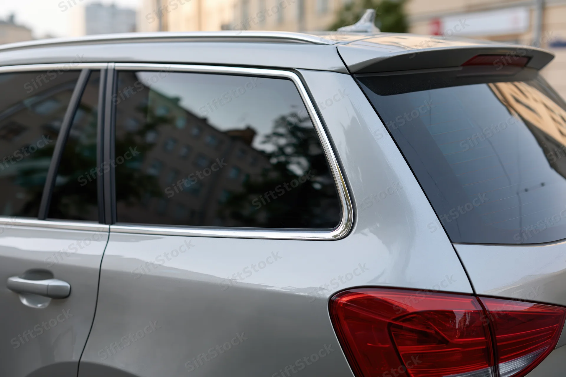 Rear view of a silver suv showing tail light and window with city reflection