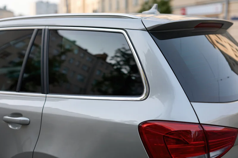 Rear view of a silver suv showing tail light and window with city reflection