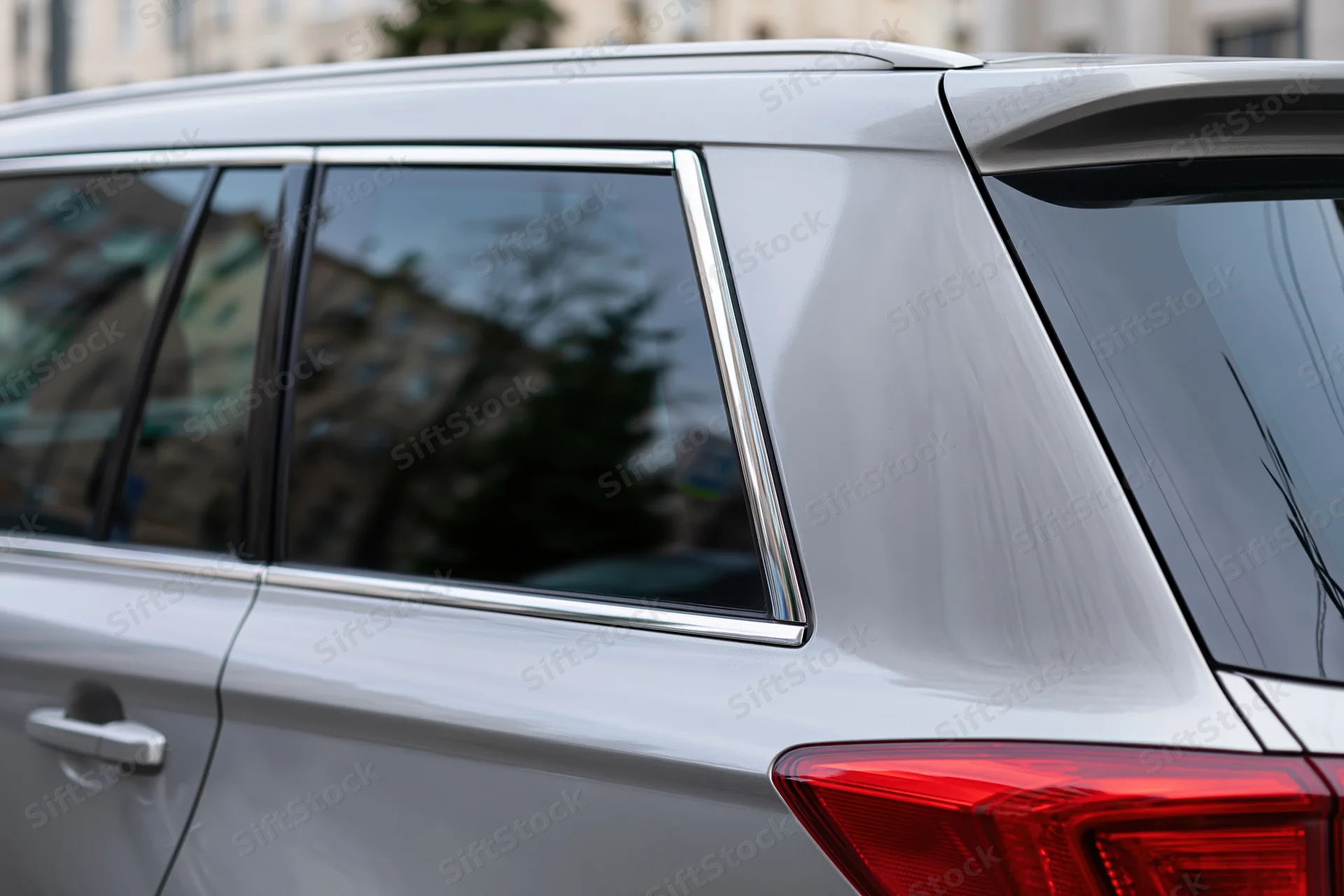 Rear window and tail light of a silver suv parked on a city street