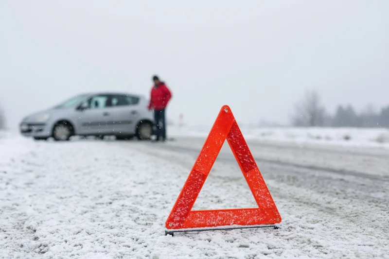 Red emergency warning triangle on snow-covered road with car and person in background