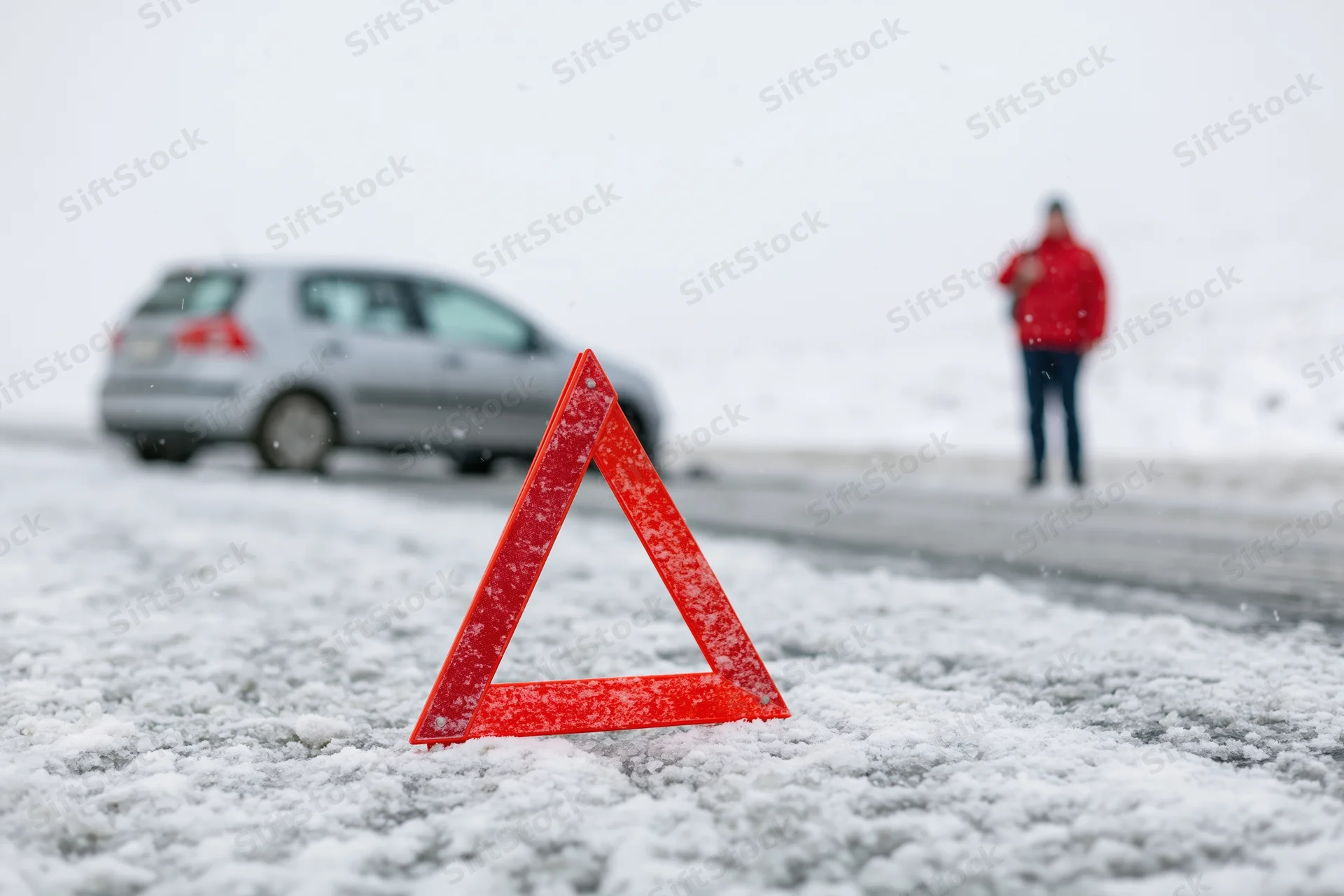 Red emergency warning triangle on snow-covered road with car and person in background