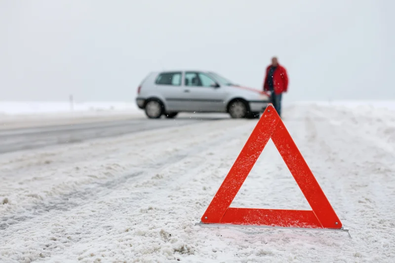 Red emergency warning triangle on snow-covered road with car and man in background