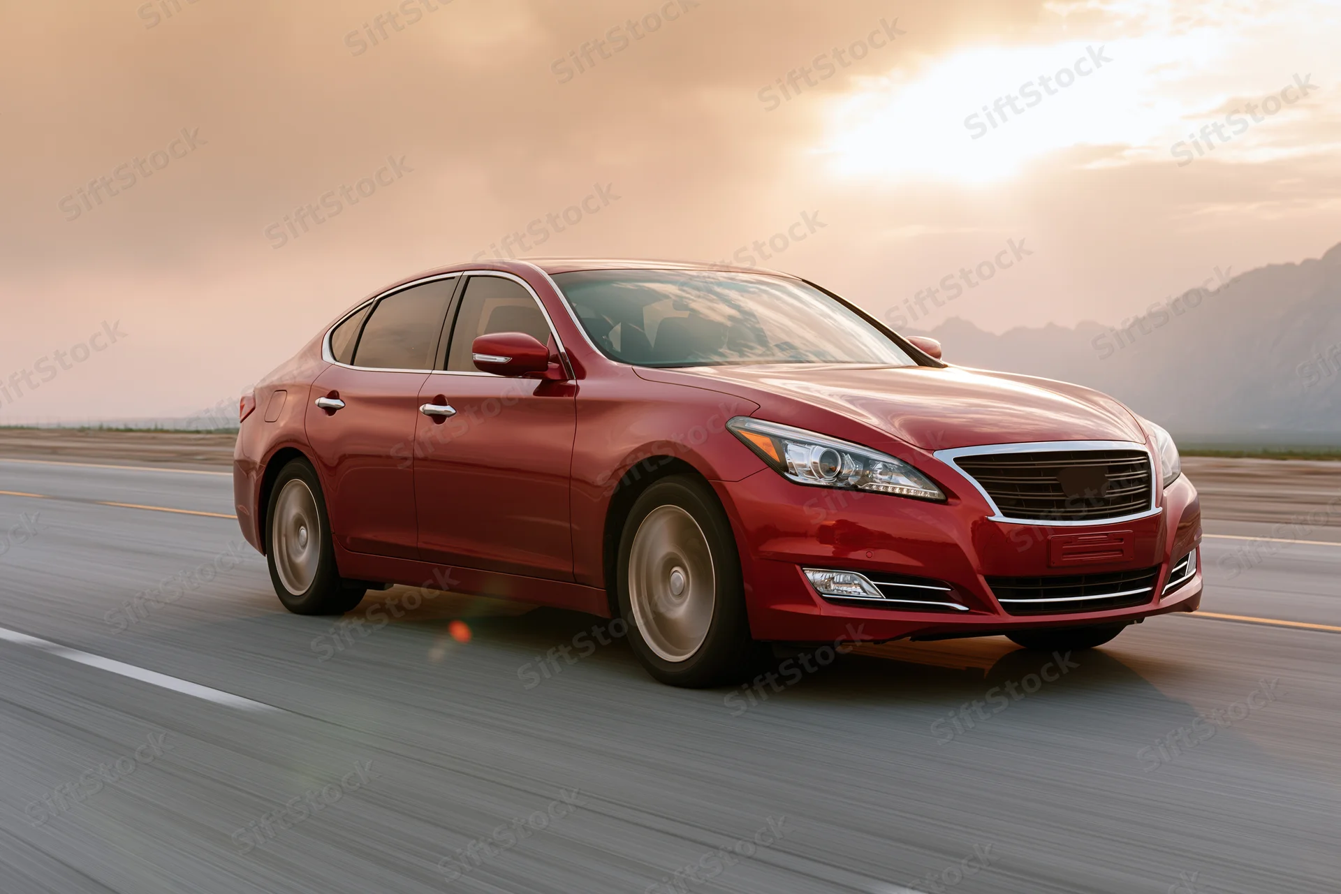 Red luxury sedan driving on open highway at sunset