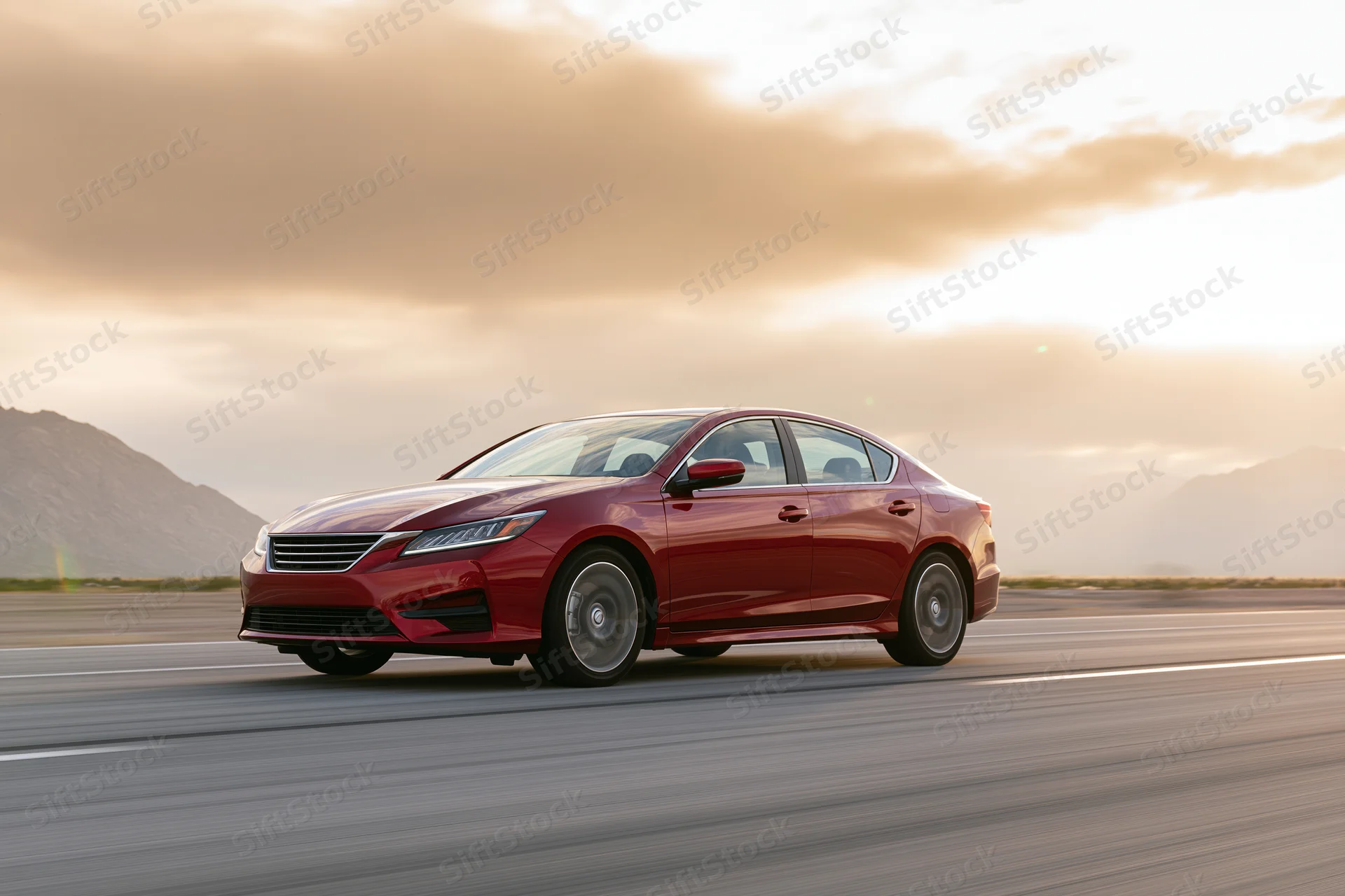 Red luxury sedan driving on open highway at sunset