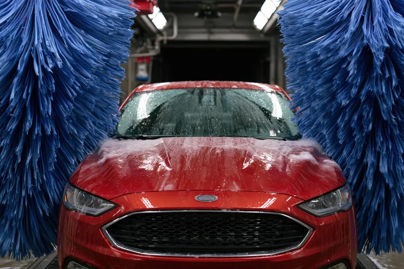 Red sedan moving through automatic car wash tunnel flanked by blue brushes