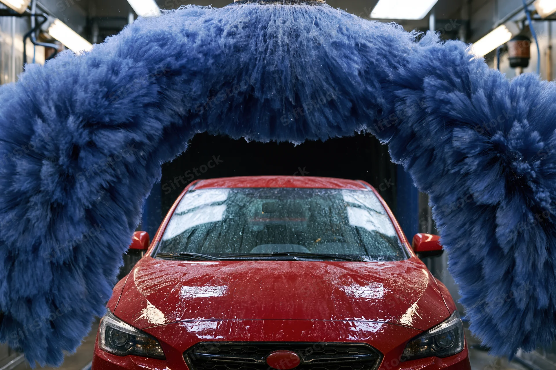 Red sedan moving through automatic car wash tunnel flanked by large blue brushes