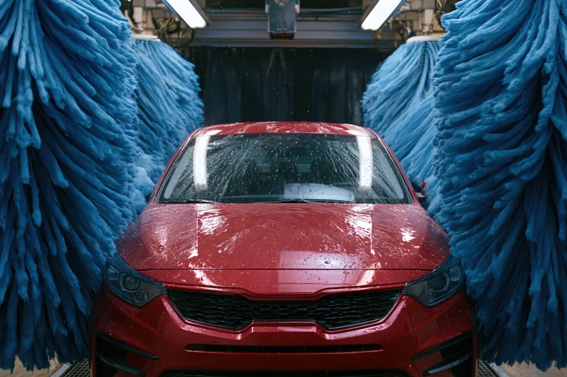 Red sedan moving through automatic car wash tunnel flanked by blue brushes