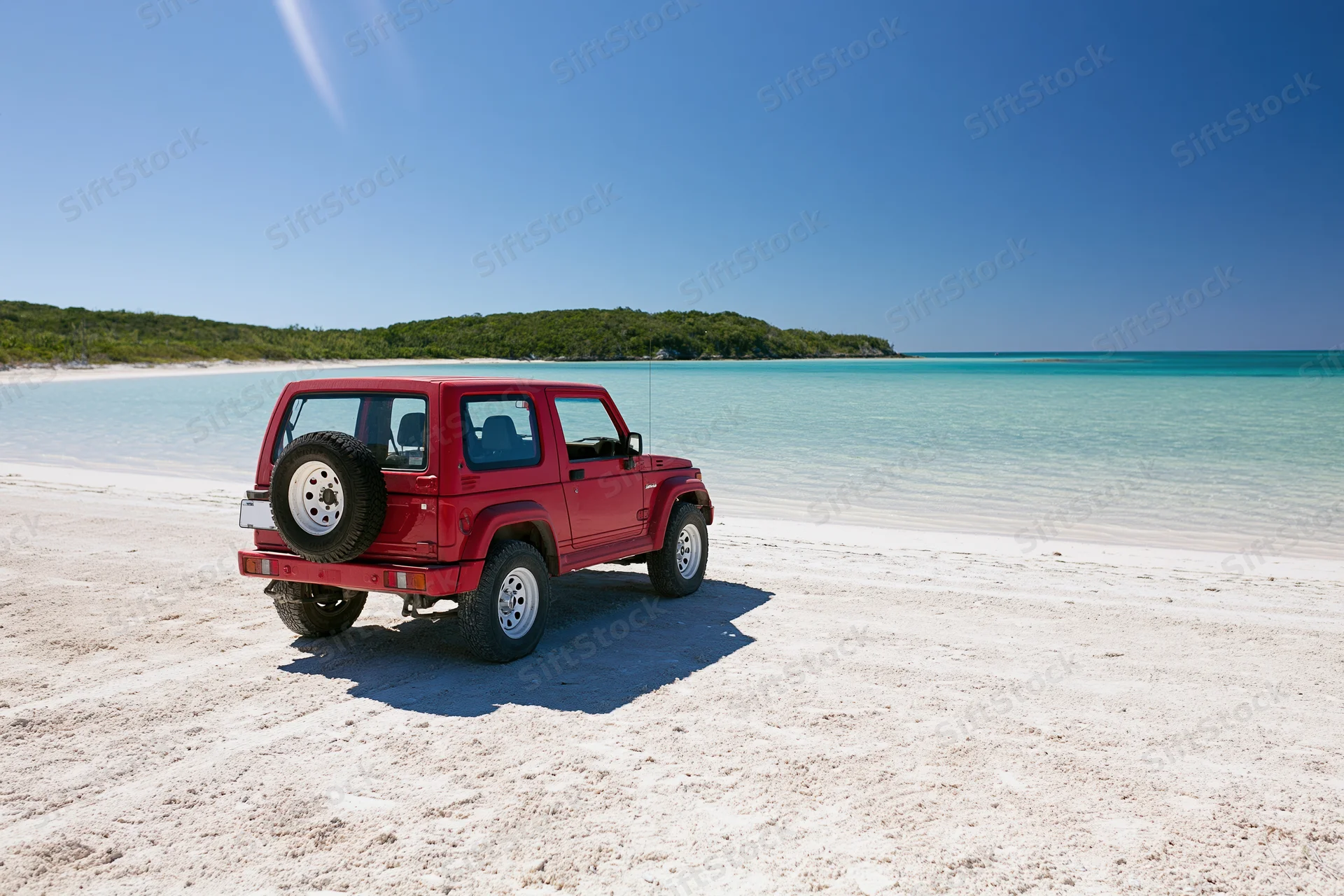 Red two-door suv parked on white sand beach facing turquoise ocean