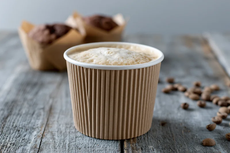 Ripple-wrap paper coffee cup filled with latte on wooden table with scattered coffee beans
