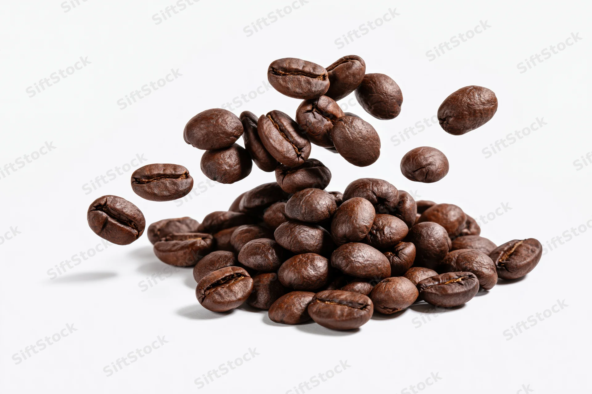 Roasted coffee beans falling and landing onto a small pile on white background
