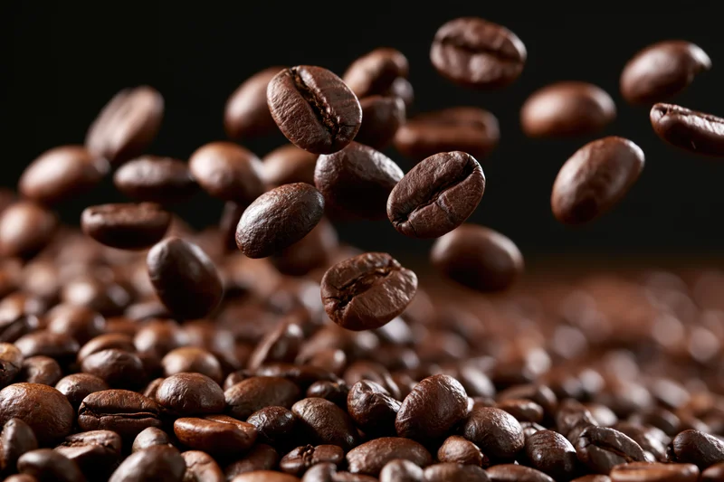 Roasted coffee beans falling and tumbling onto a pile against a dark background